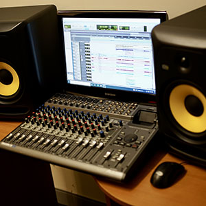 Photo of recording software on a computer surrounded by speakers.