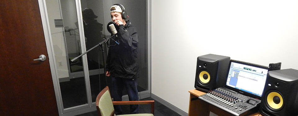 Photo of a student recording himself singing on a microphone.