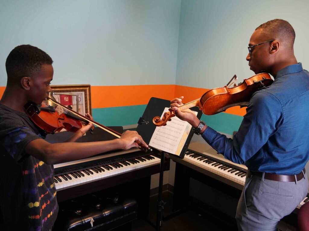 Photo of a student practicing violin with their teacher.