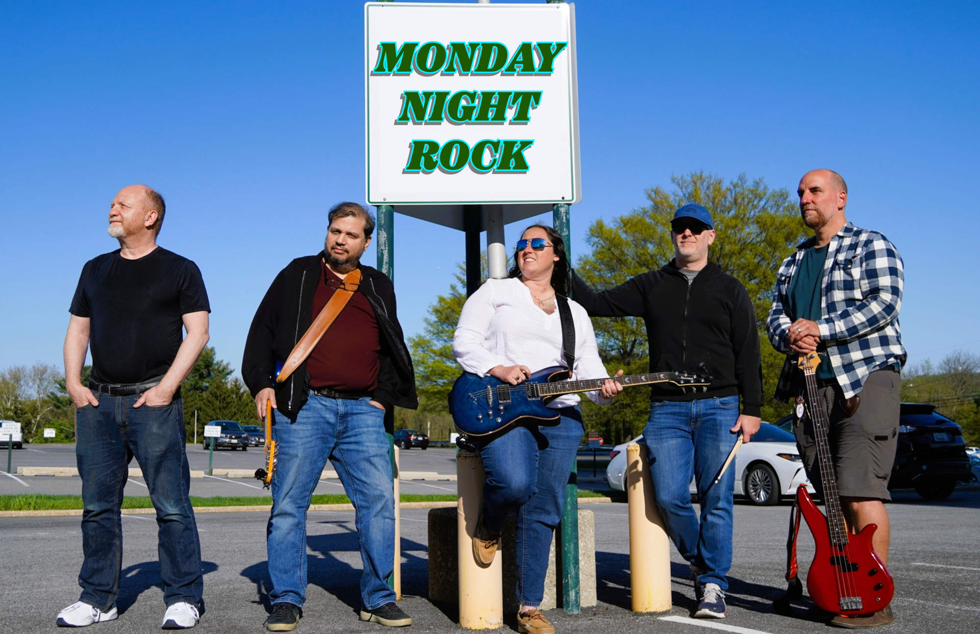 Students posing with their instruments with the words "Monday Night Rocks" on a sign behind them.