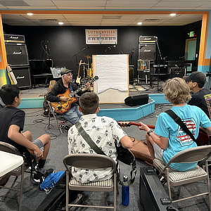 Students with guitars sit in a circle with a teacher.