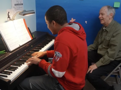 Piano Photo of a piano student practicing while their teacher assists.