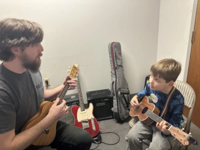 Ukulele Photo of a student being taught the ukulele by their teacher.